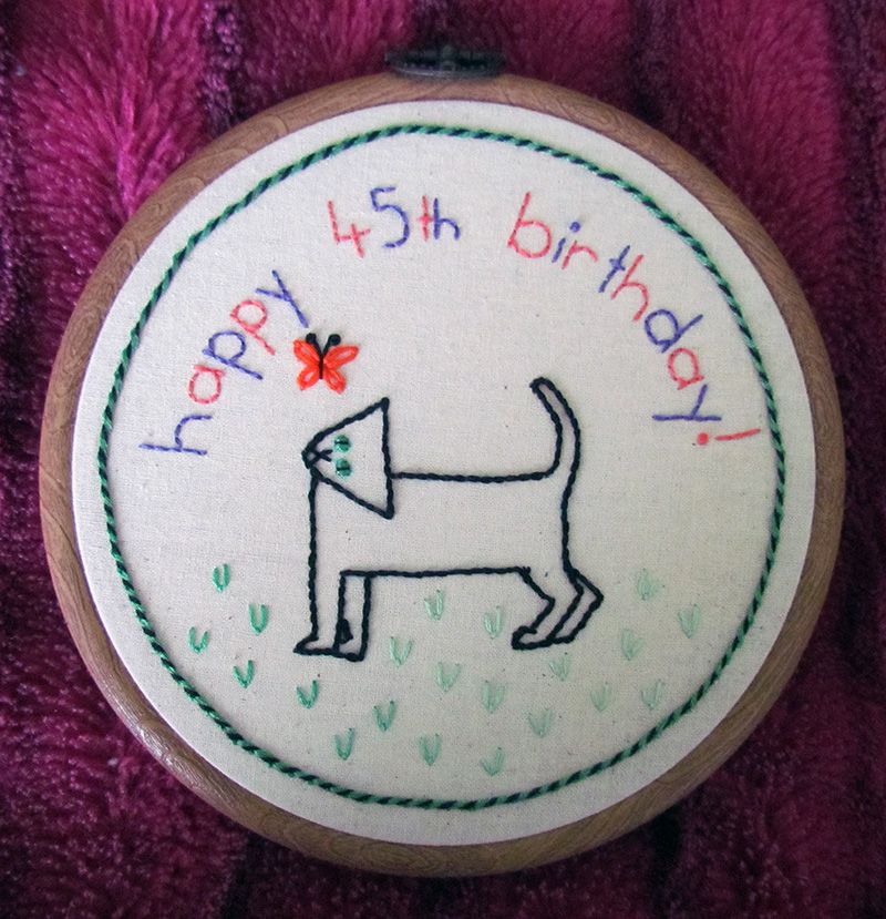 Embroidered medallion with black cat looking at a butterfly and a whipped chain stitch border