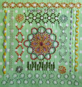 Embroidered running stitch sampler on green fabric with white spots.