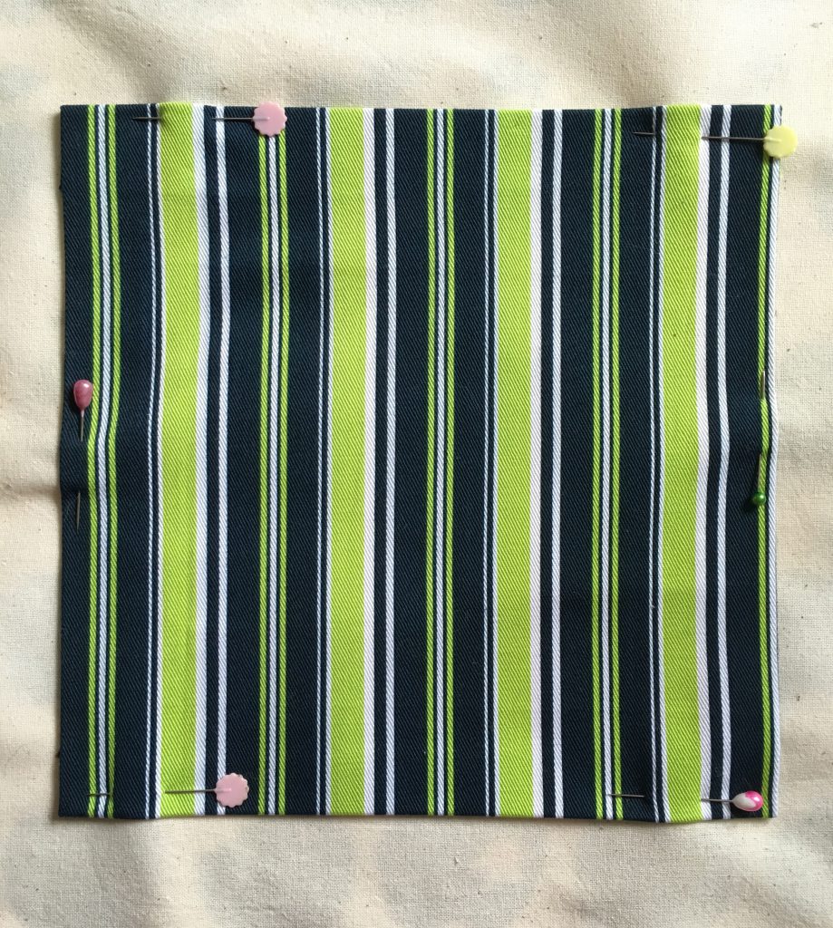 A square of navy blue, lime and white striped twill cotton fabric pinned to a background of unbleached calico.
