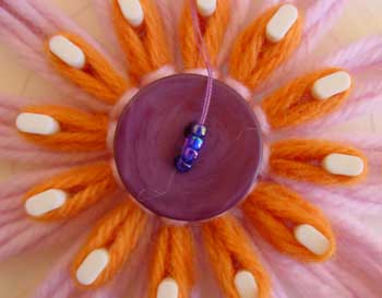 Stitching a button to the center of a loomed flower