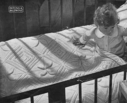 Baby in a cot with a hand knit bedspread with lace and embossed leaf design.