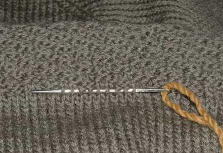 Darning needle threaded with a length of yarn being used to capture the stitches so they don't unravel.