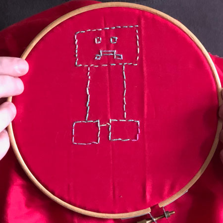 An embroidered Minecraft creeper on red polycotton