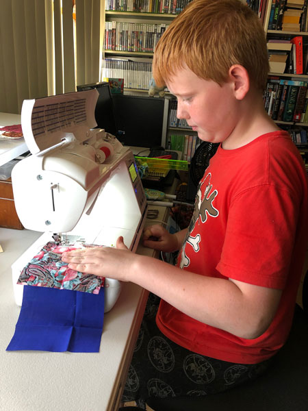 10 year old boy sitting at a sewing machine, making a piece of patchwork.