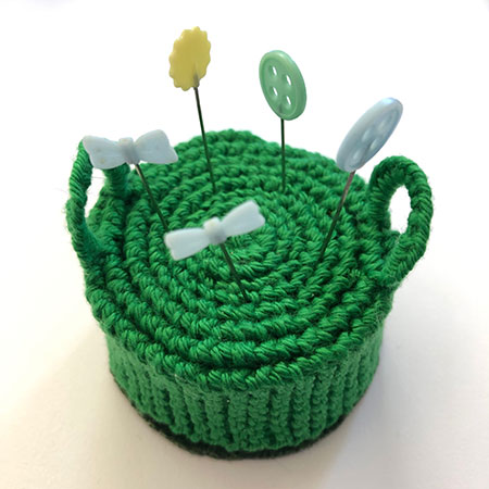 Hand knit pincushion in the shape of an Edwardian hassock with handles