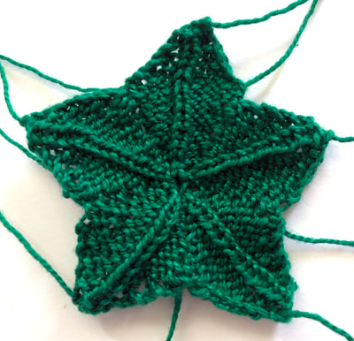 A green, star shaped piece of knitting used to form the leaves on the strawberry pincushion.