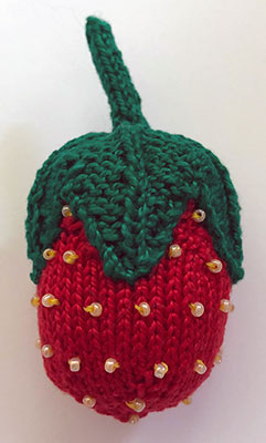A hand knit pincushion in the shape of a strawberry
