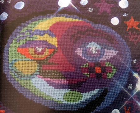 Needlepoint design showing the moon in flat areas of colour, with mirrors attached to represent stars.