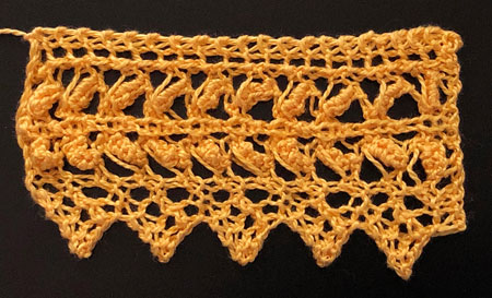 A yellow knitted lace edging with wide open bands of textured lace and a pointed edge