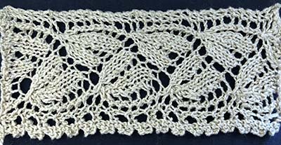 Knitted sample of wheat pattern edging with a band of floral motifs and frilly edge.