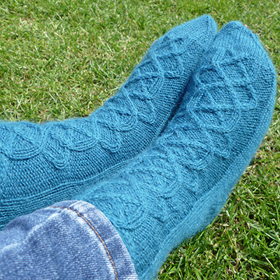 Blue, mid-calf length socks with a wide cable pattern up the front that goes from the ribbed cuff  
to the toe decreases. 