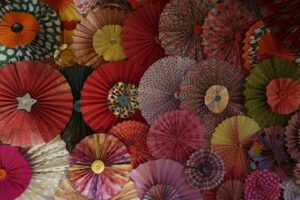 Colourful paper rosettes made by accordion folding paper.  The ridges  of the folds radiate out from the centre like sun rays. 
