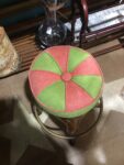 A pink and green upholstered, circular stool with 8 wedges of alternating colours.